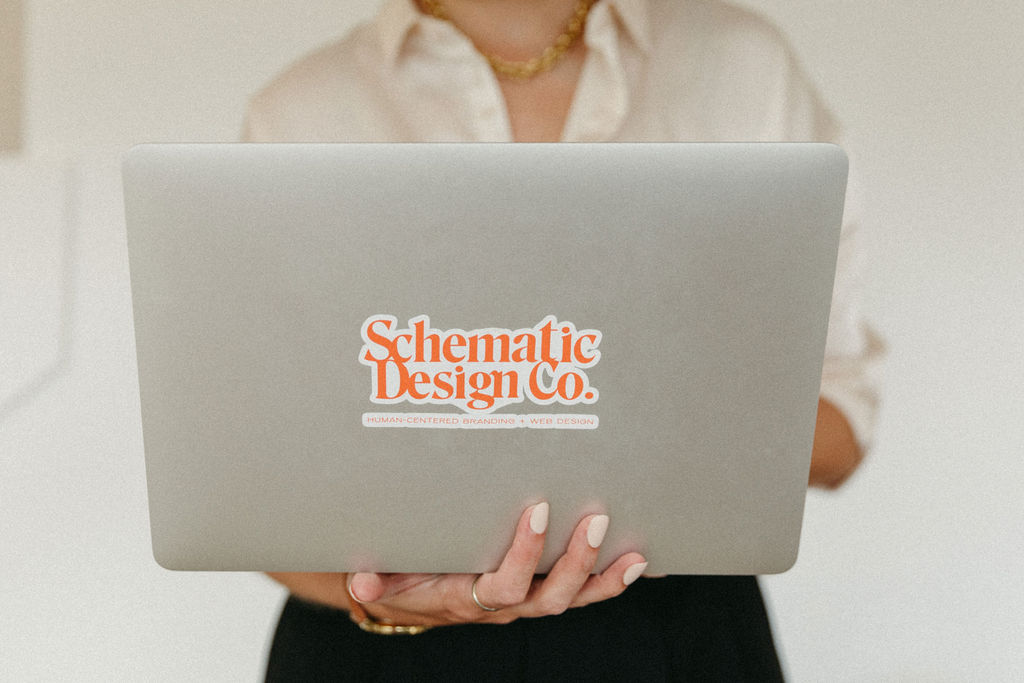 Brand designer Carly holds a MacBook Pro with the new Schematic logo design on the back